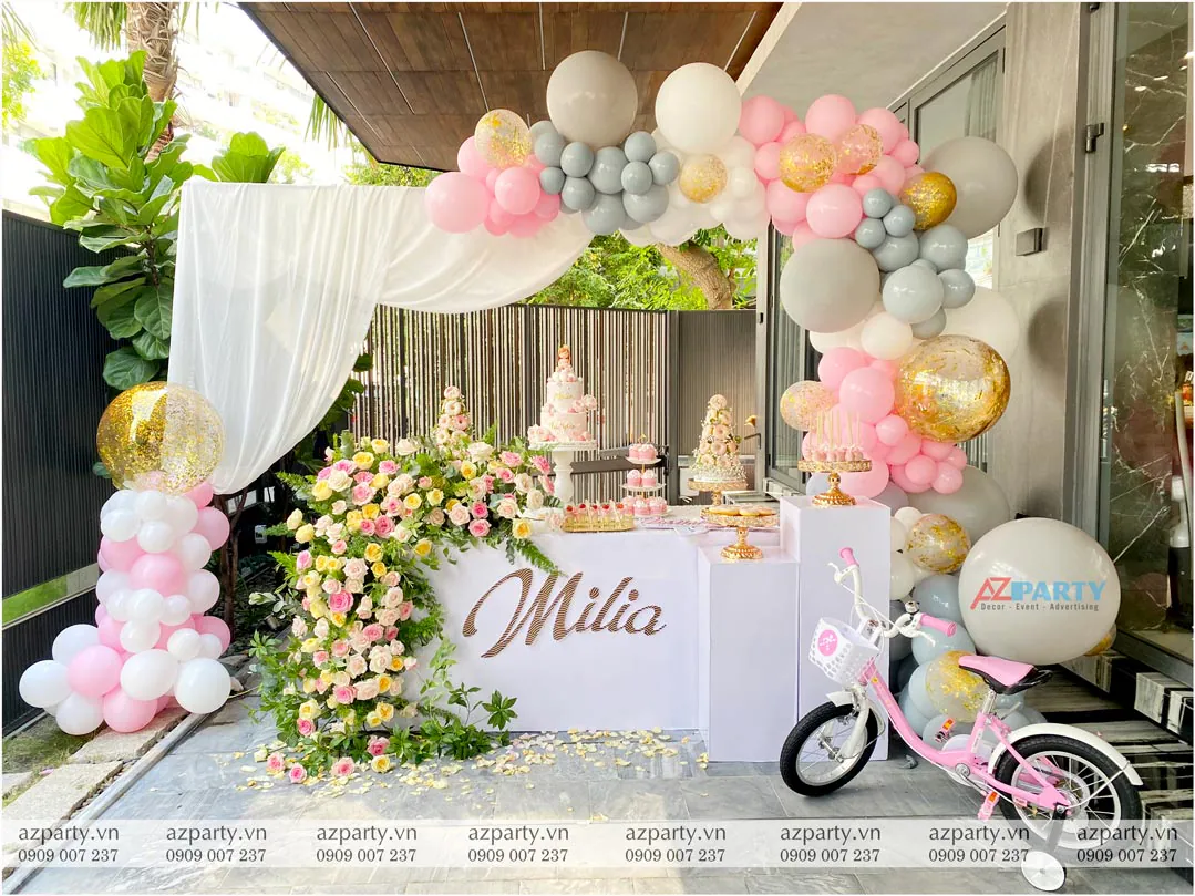 Không gian trang trí tiệc sinh nhật bé Milia ngoài trời tinh tế với bàn gallery phủ hoa tươi rực rỡ và cổng bong bóng tông hồng pastel lãng mạn.