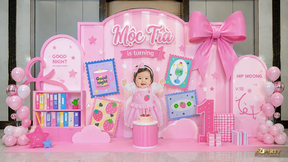 Backdrop màu hồng sọc với nơ lớn, kệ sách, tranh dâu tây và ảnh bé