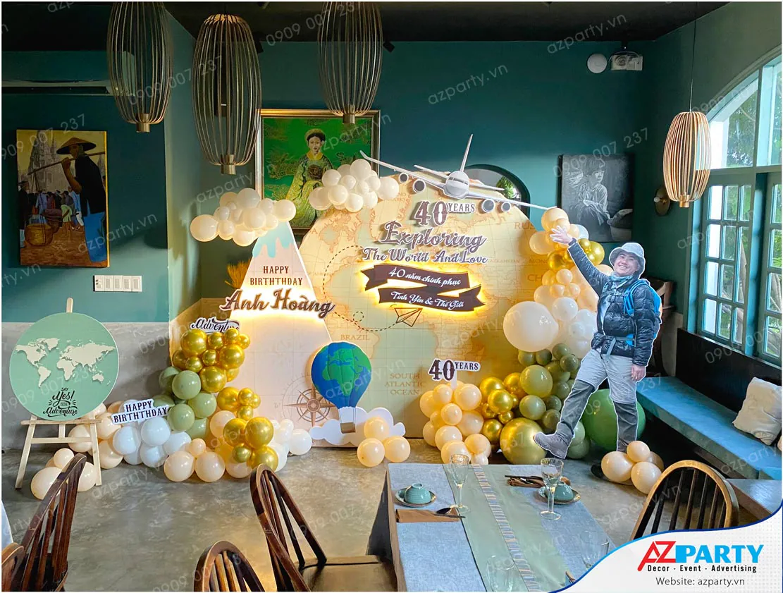 Trang trí tiệc sinh nhật người lớn tuổi 40 chủ đề du lịch thế giới (Travel the World) với backdrop bản đồ thế giới cổ điển, mô hình máy bay và standee chủ tiệc phong cách phượt thủ.