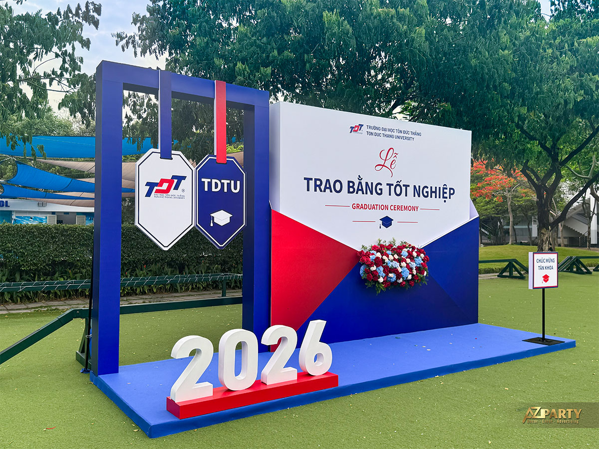 Góc nghiêng Booth 1 Graduation Ceremony ĐH Tôn Đức Thắng với bục sân khấu xanh và chữ 2026 nổi bật