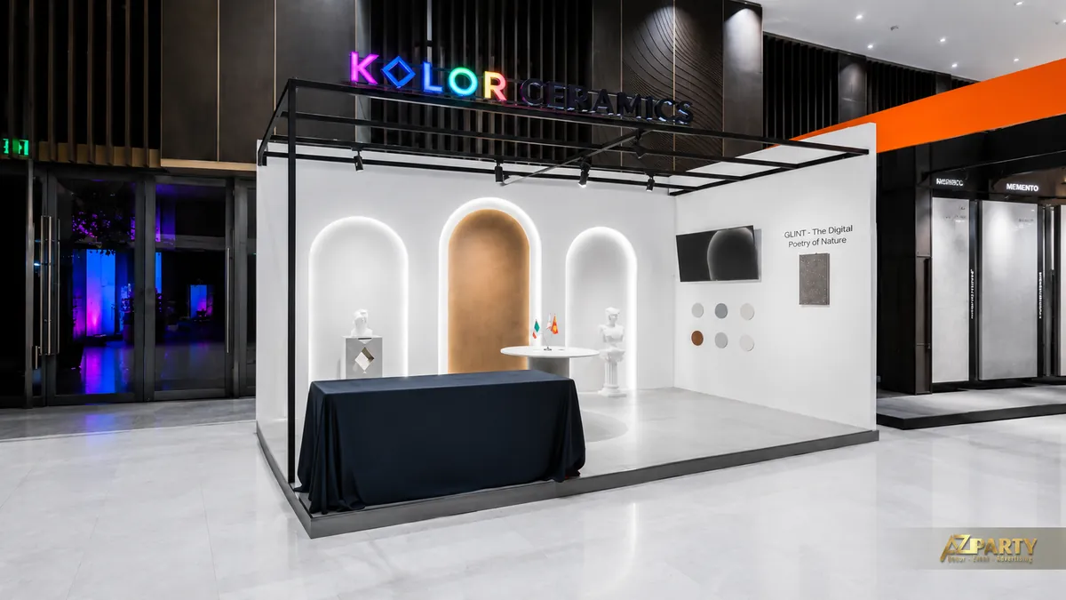 Góc nghiêng booth Kolor Ceramics với khung đen phía trên, logo LED và khu trưng bày GLINT bên phải