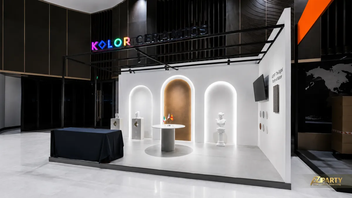 Góc nhìn bên trái booth Kolor Ceramics với hệ vòm đèn, bàn trưng bày trung tâm và vách giới thiệu GLINT