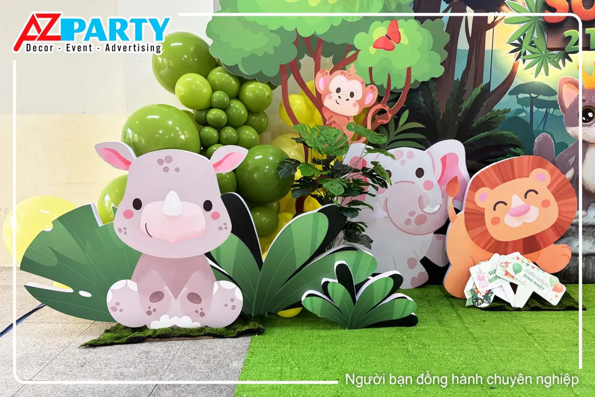 Góc trang trí bên trái của sân khấu sinh nhật chủ đề rừng safari với mô hình tê giác hồng, voi con, sư tử dễ thương cùng chùm bóng bay tone màu xanh lá cây.