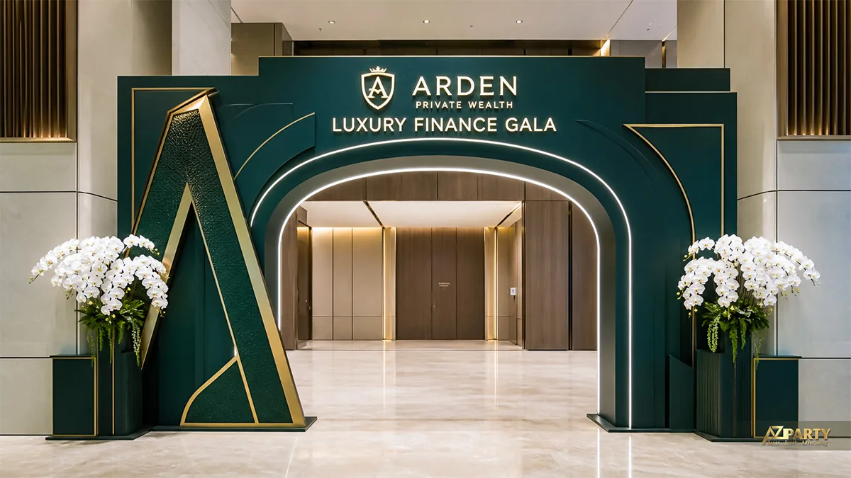 Cổng sự kiện Arden Finance xanh đậm viền vàng, chữ A cách điệu và hai chậu lan trắng