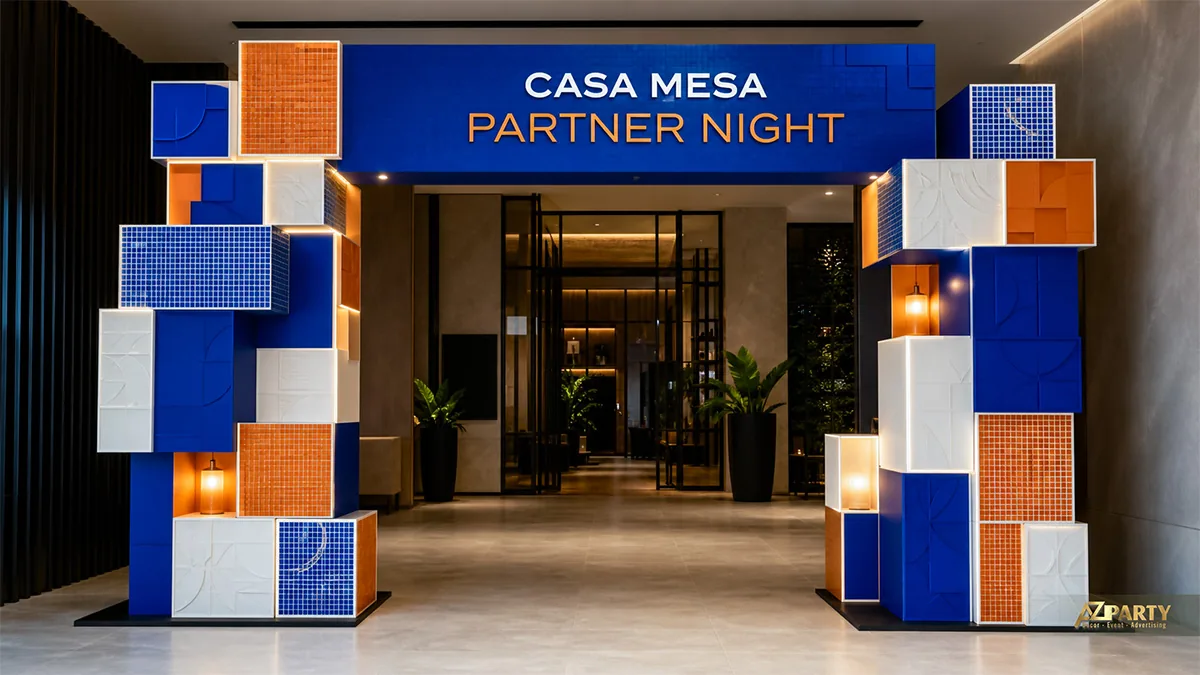Cổng Partner Night Casa Mesa ghép từ nhiều khối vuông xanh, cam, trắng và đèn hắt