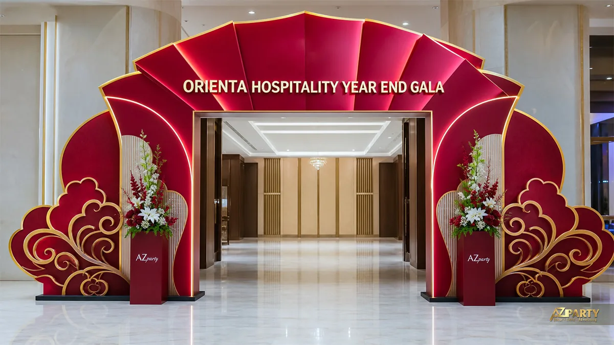 Cổng chào gala Orienta màu đỏ đô viền vàng, tạo hình nan quạt và mây cách điệu kèm hai trụ hoa