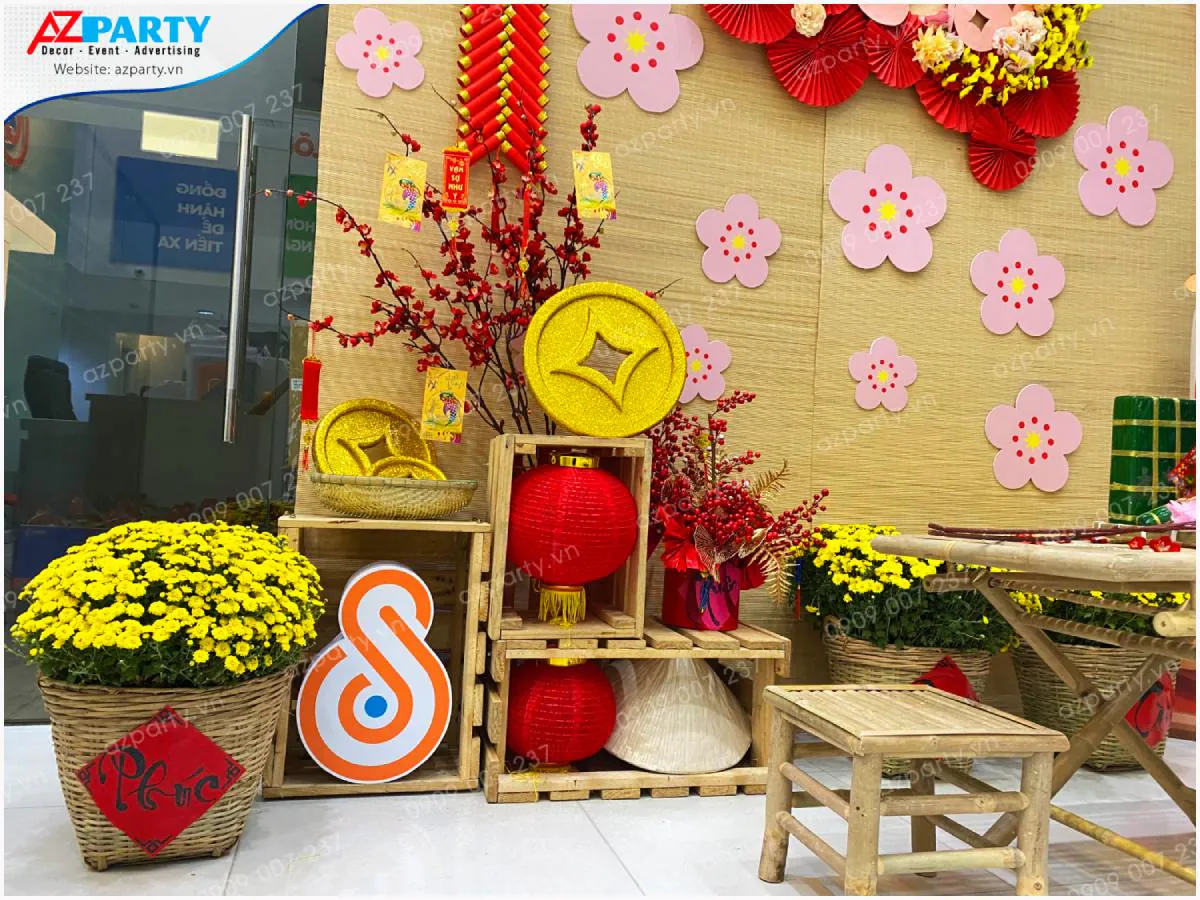 Các phụ kiện trang trí Tết cổ truyền như đèn lồng đỏ, bánh chưng xanh, đồng tiền vàng, nón lá và chậu hoa cúc mâm xôi đặt trên kệ gỗ mộc mạc
