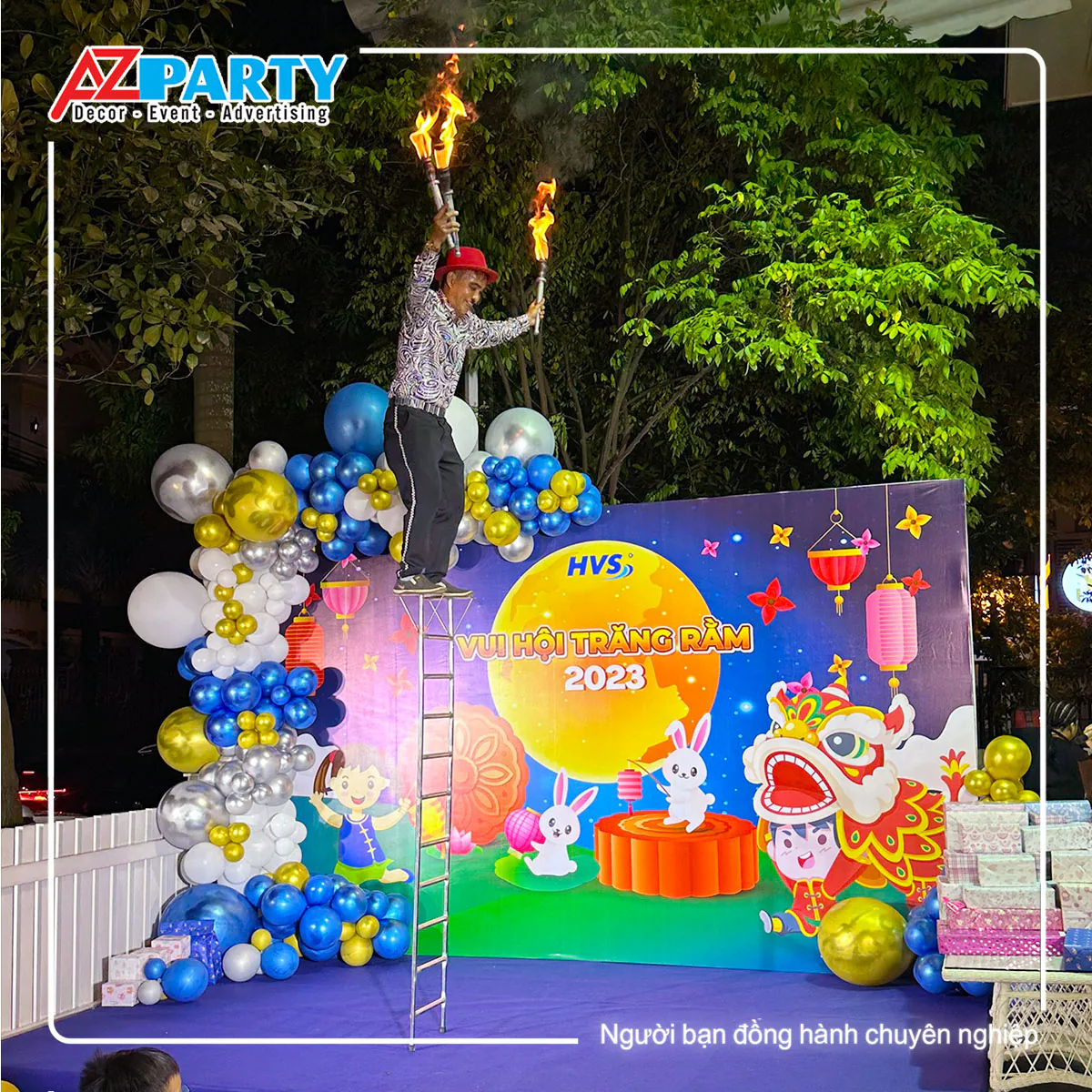 Nghệ sĩ xiếc biểu diễn thăng bằng trên thang cao với đuốc lửa trước backdrop Vui Hội Trăng Rằm 2023 HVS