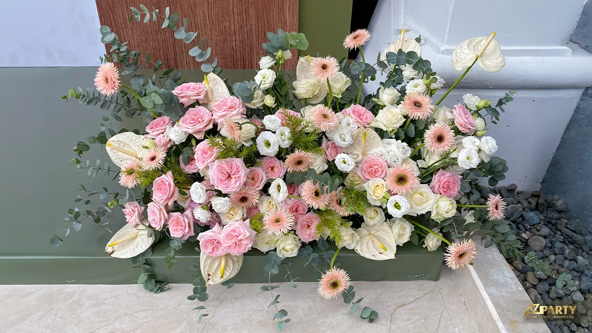 Cụm hoa tươi đặt chân backdrop Maison Mama với hoa hồng pastel, hoa đồng tiền và nền xanh sage
