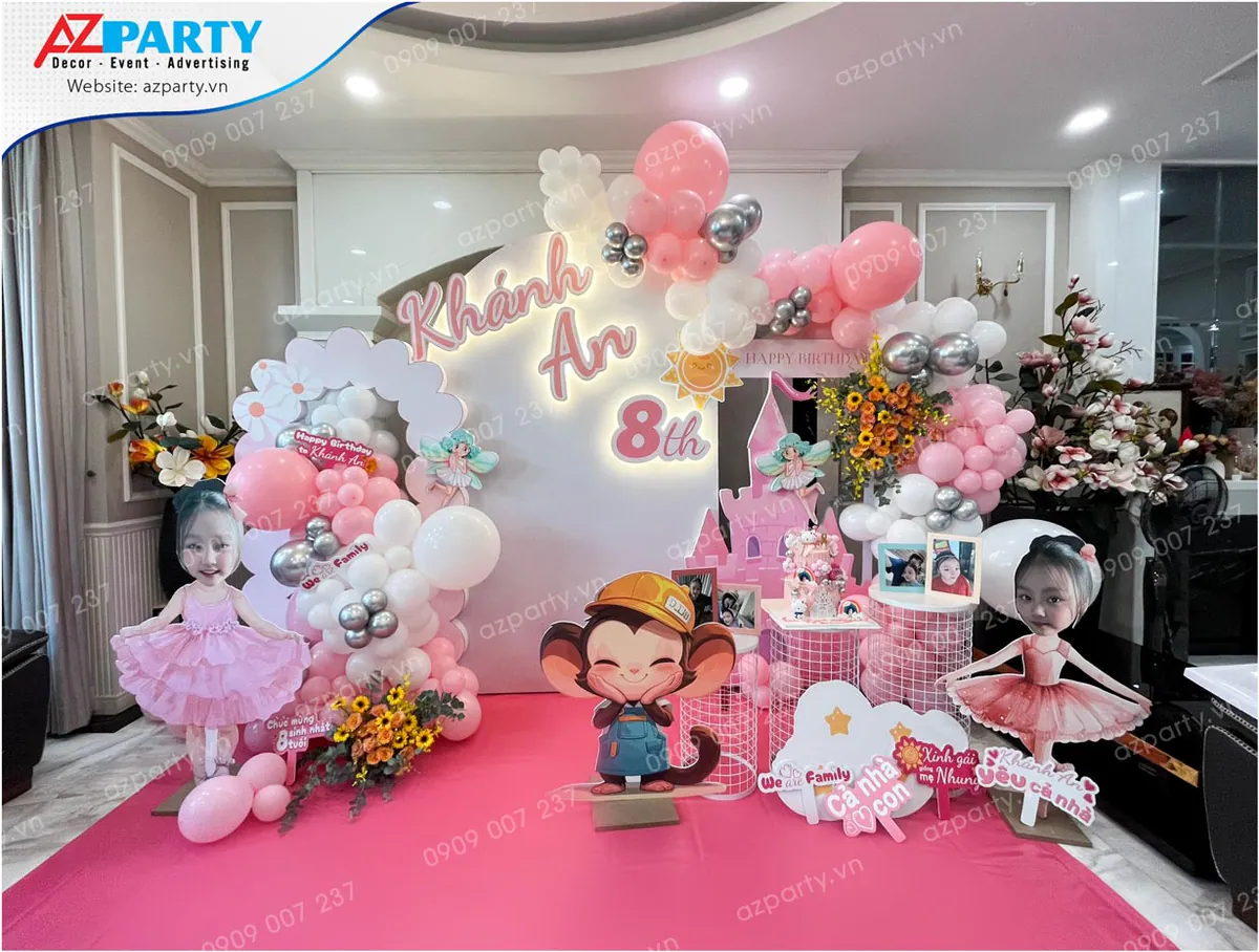 Trang trí tiệc sinh nhật bé Khánh An tròn 8 tuổi với tone màu hồng mộng mơ chủ đạo, kết hợp cổng bóng bay nghệ thuật hồng trắng bạc, các mô hình chibi bé mặc váy múa ballet dễ thương và hình chú khỉ đội mũ bảo hộ ở trung tâm.