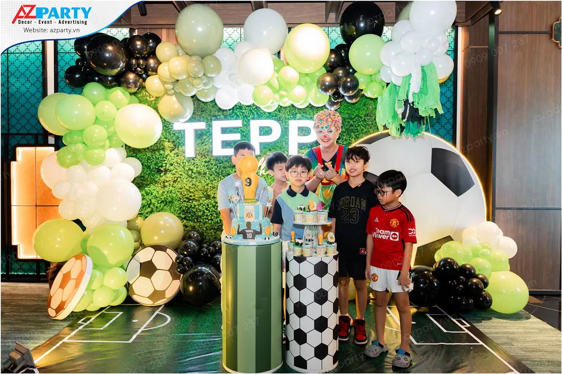 Bé Teppi cùng các bạn nhỏ chụp ảnh kỷ niệm bên chú hề MC tại khu vực sân khấu sinh nhật 9 tuổi chủ đề bóng đá chuyên nghiệp.