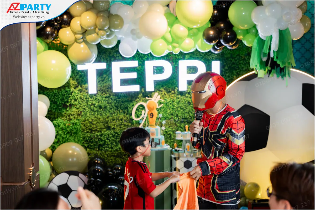 Nghệ sĩ hóa trang Iron Man mang mặt nạ vàng đỏ đang biểu diễn ảo thuật tương tác cùng các bé trên sân khấu tiệc sinh nhật bé Teppi.