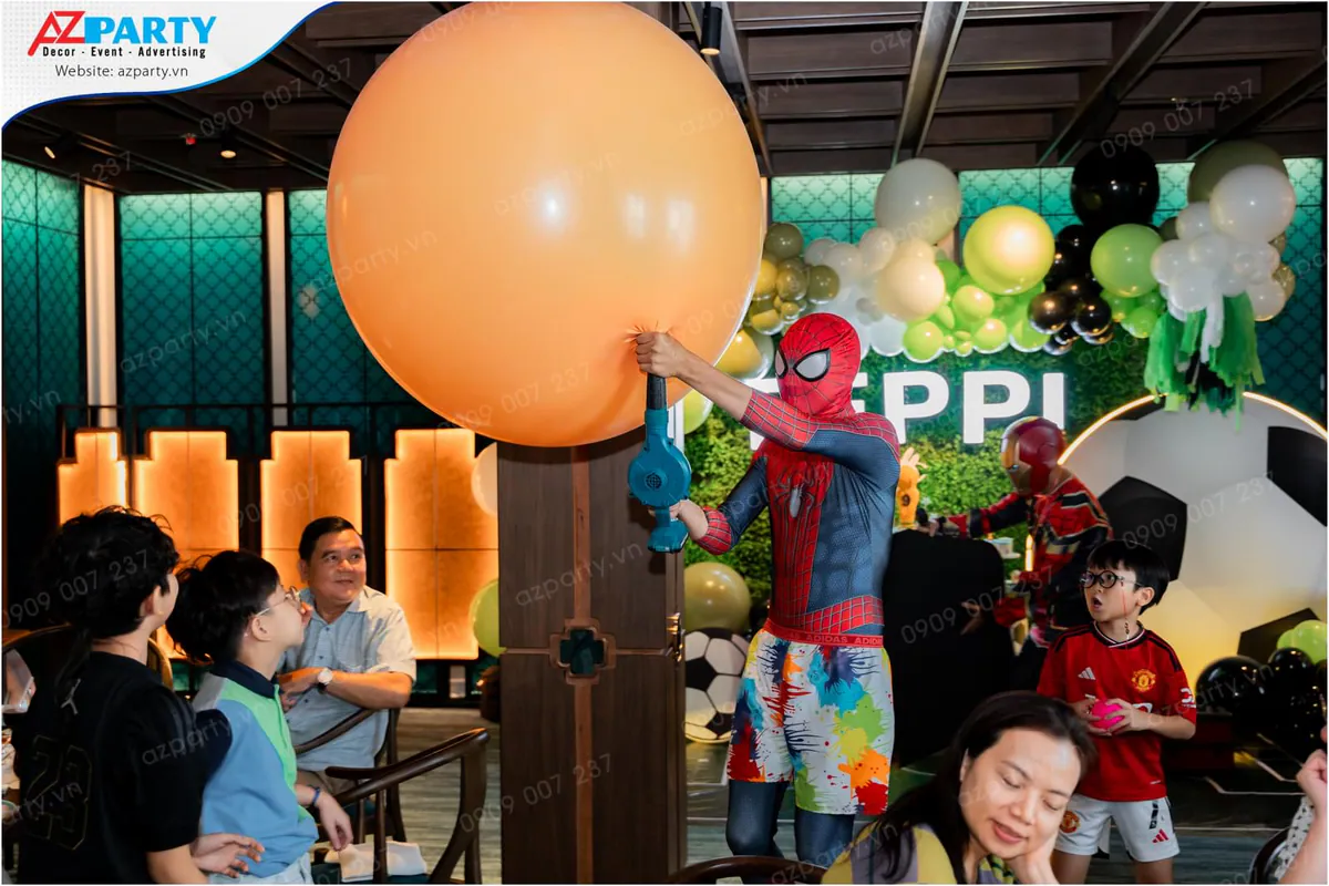 Nghệ sĩ người nhện Spider-Man đang biểu diễn bơm quả bóng bay màu cam khổng lồ trước sự phấn khích của các khách mời tại bữa tiệc.