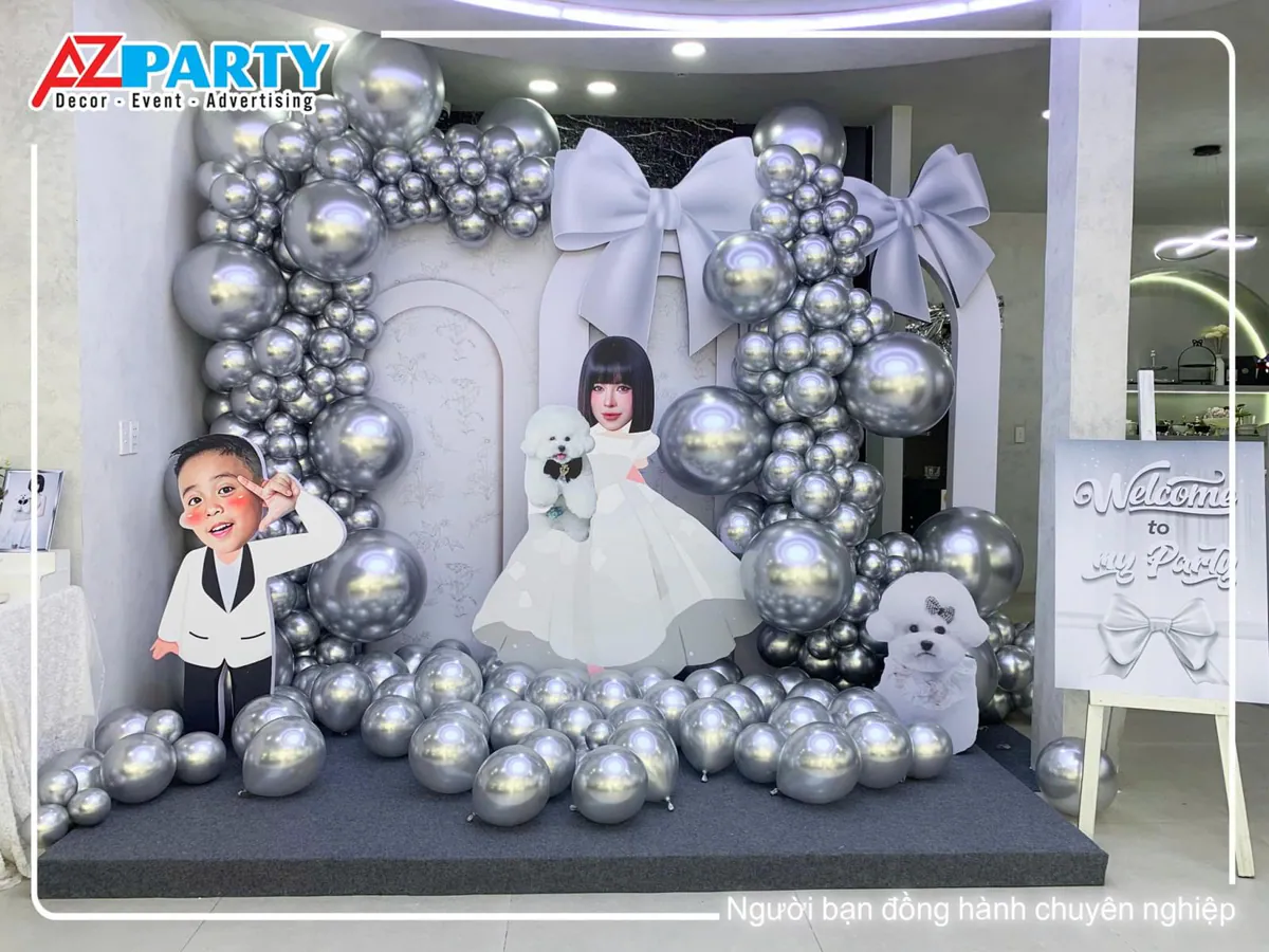 Sân khấu photobooth trang trí sinh nhật tại nhà sang trọng với bong bóng màu bạc chrome và mô hình chibi gia đình dễ thương