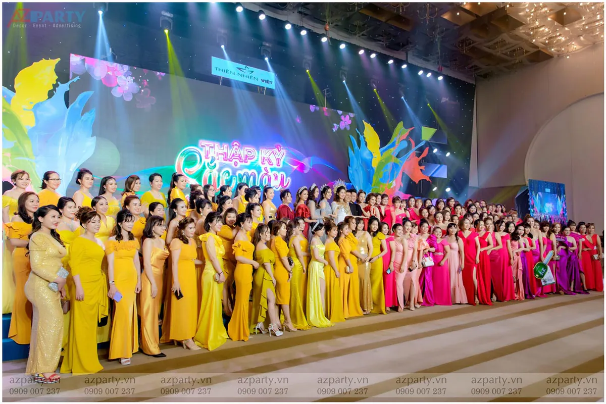 Dàn khách mời đông đảo mặc váy đầm đồng điệu tông vàng và đỏ chụp ảnh lưu niệm trên sân khấu đêm dạ tiệc Thiên Nhiên Việt.
