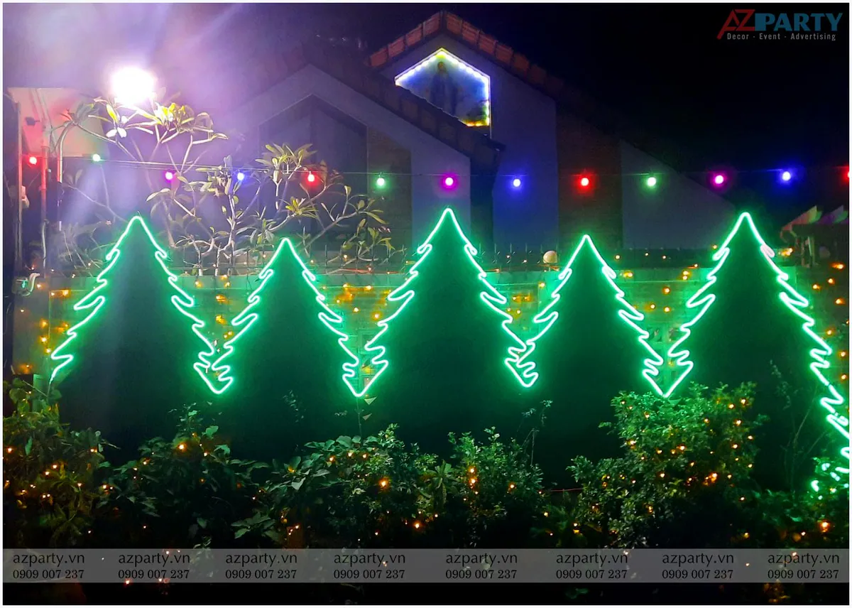 Hàng rào nhà riêng trang hoàng Giáng sinh bằng đèn neon uốn hình cây thông Noel màu xanh lá cây rực rỡ và các bụi cây chăng đèn led vàng ấm áp
