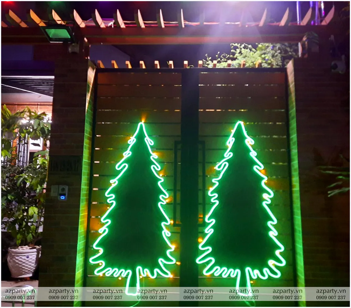 Cận cảnh hai cây thông Noel bằng đèn neon uốn nghệ thuật phát ánh sáng xanh lá cây nổi bật trên cánh cổng gỗ nhà riêng vào ban đêm