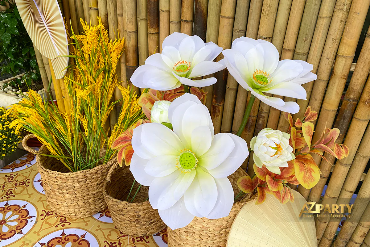 Giỏ mây đựng lúa vàng và hoa sen trắng trang trí Tết đặt trước nền tre trúc, kết hợp quạt lá và họa tiết gạch bông truyền thống.