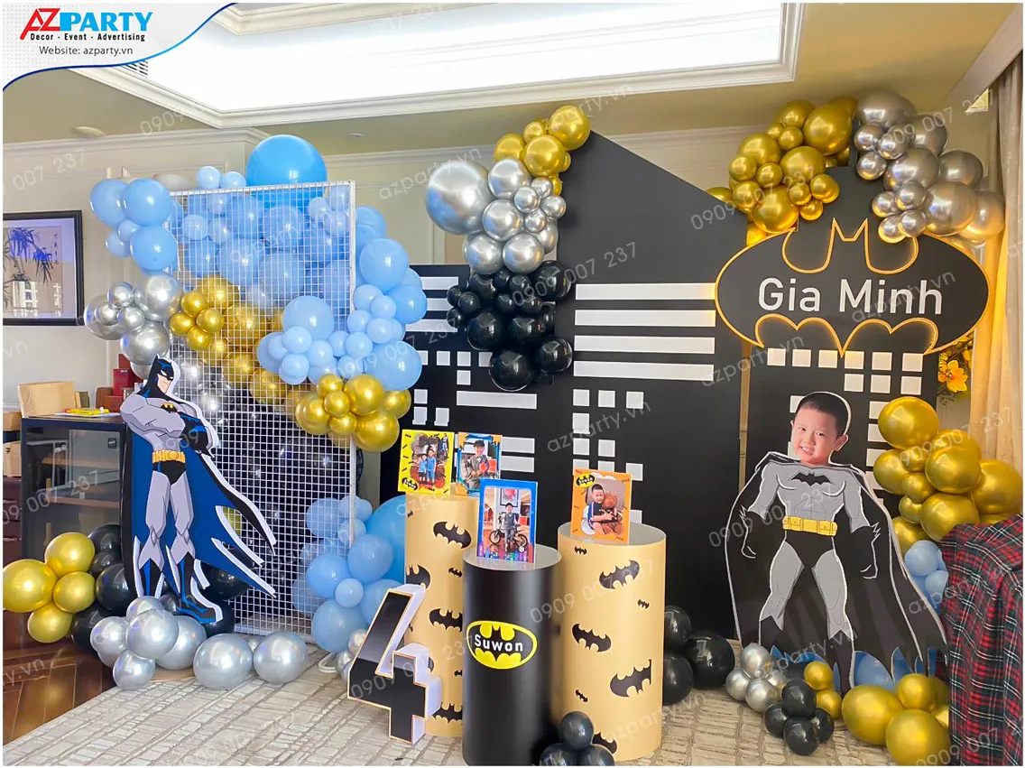 Góc chụp chính diện sân khấu Batman nổi bật với mô hình thành phố Gotham về đêm, số 4 đèn marquee và cổng bong bóng pastel.