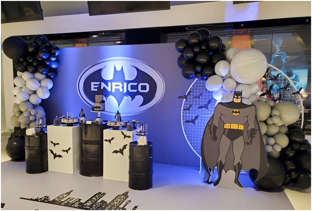 Không gian trang trí tiệc sinh nhật chủ đề Batman độc đáo cho bé Enrico với các đôn thùng phi màu đen và logo tên bé rọi đèn LED xanh.
