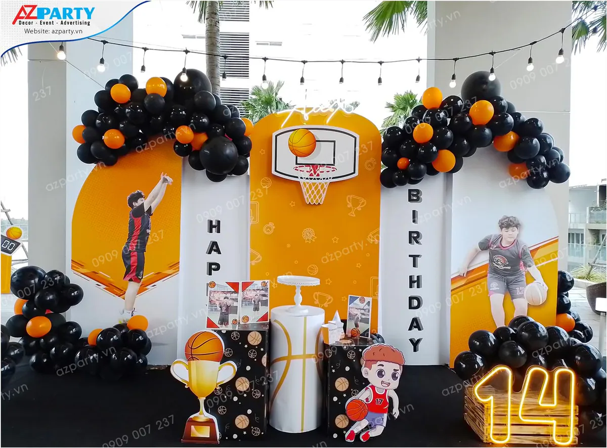 Cận cảnh khu vực backdrop chính của tiệc sinh nhật Alex 14 tuổi với chiếc cúp vàng biểu tượng, nhân vật hoạt hình chơi bóng rổ và số 14 phát sáng rực rỡ.