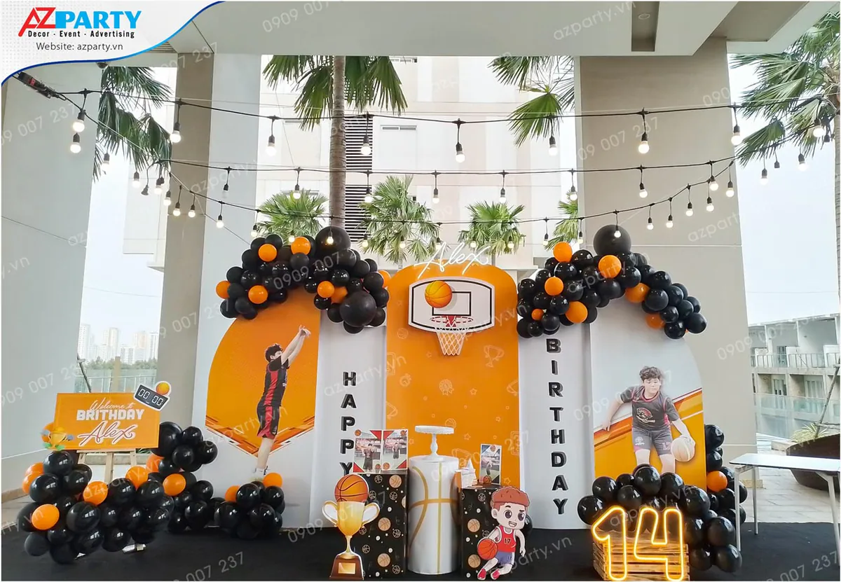 Trang trí tiệc sinh nhật ngoài trời chủ đề bóng rổ cho bé Alex tròn 14 tuổi với backdrop in hình bé đang chơi bóng, rổ ném bóng, chữ số 14 gắn đèn LED sáng ấm áp cùng bóng bay đen và cam.