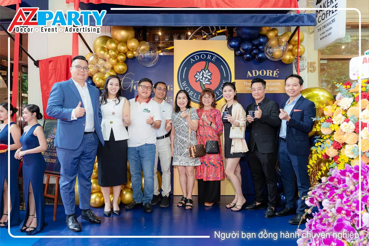 Khách mời chụp ảnh kỷ niệm trước backdrop khai trương sang trọng của Adore World Coffee.