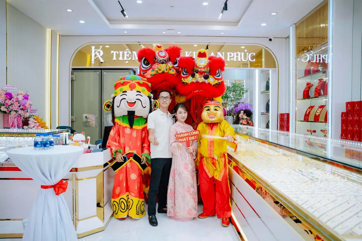 1 nhân sự nam và nhân sự nữ của Kim An Phúc chụp hình cùng ông thần tài và ông địa trong không cửa hàng