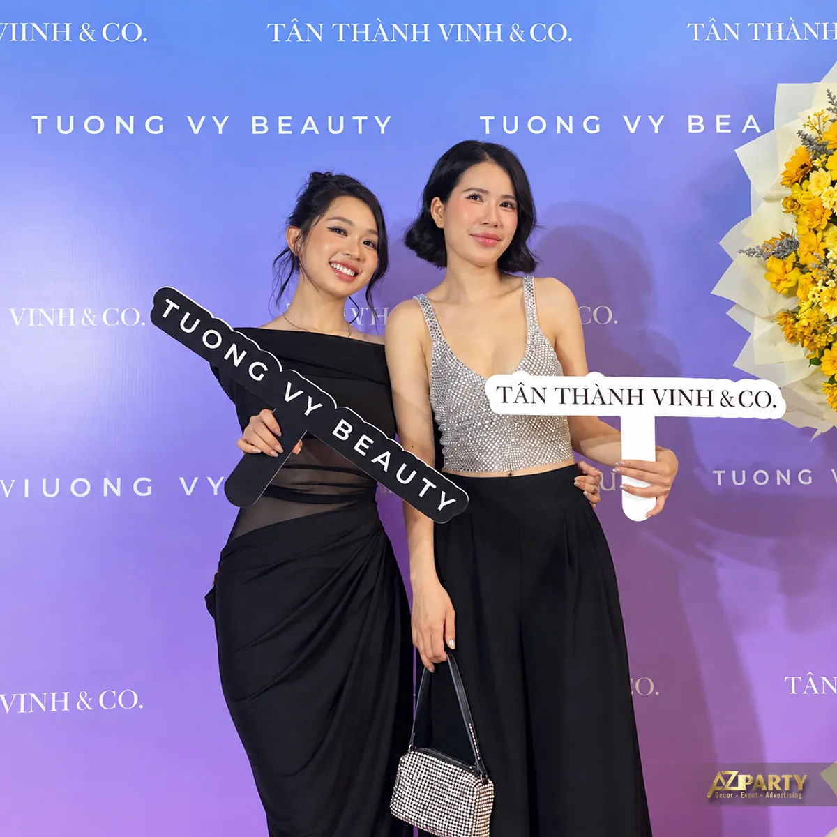 Khách mời cầm bảng thương hiệu trước backdrop tím
