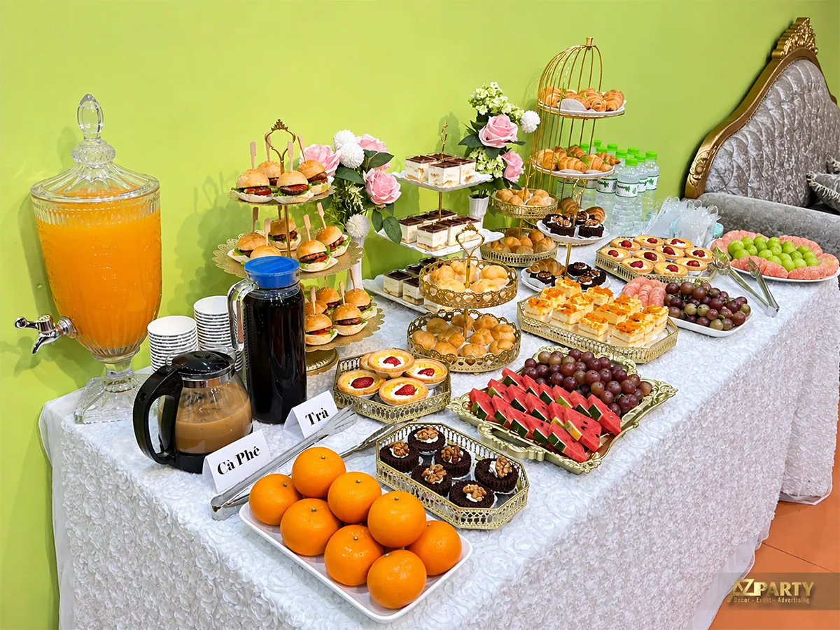 Bàn tiệc trà trước tường xanh với bánh, trái cây và đồ uống
