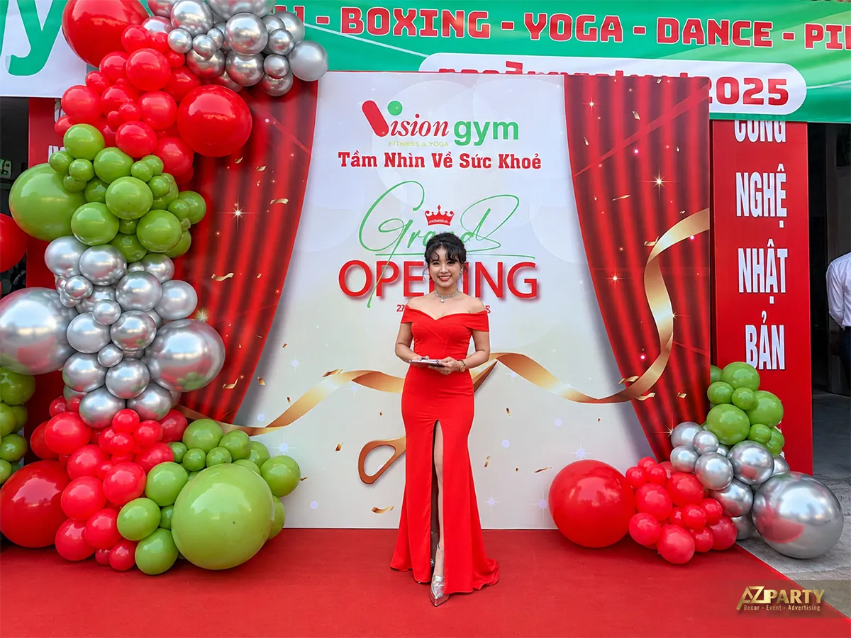 Người dẫn chương trình mặc váy đỏ trước backdrop Vision Gym
