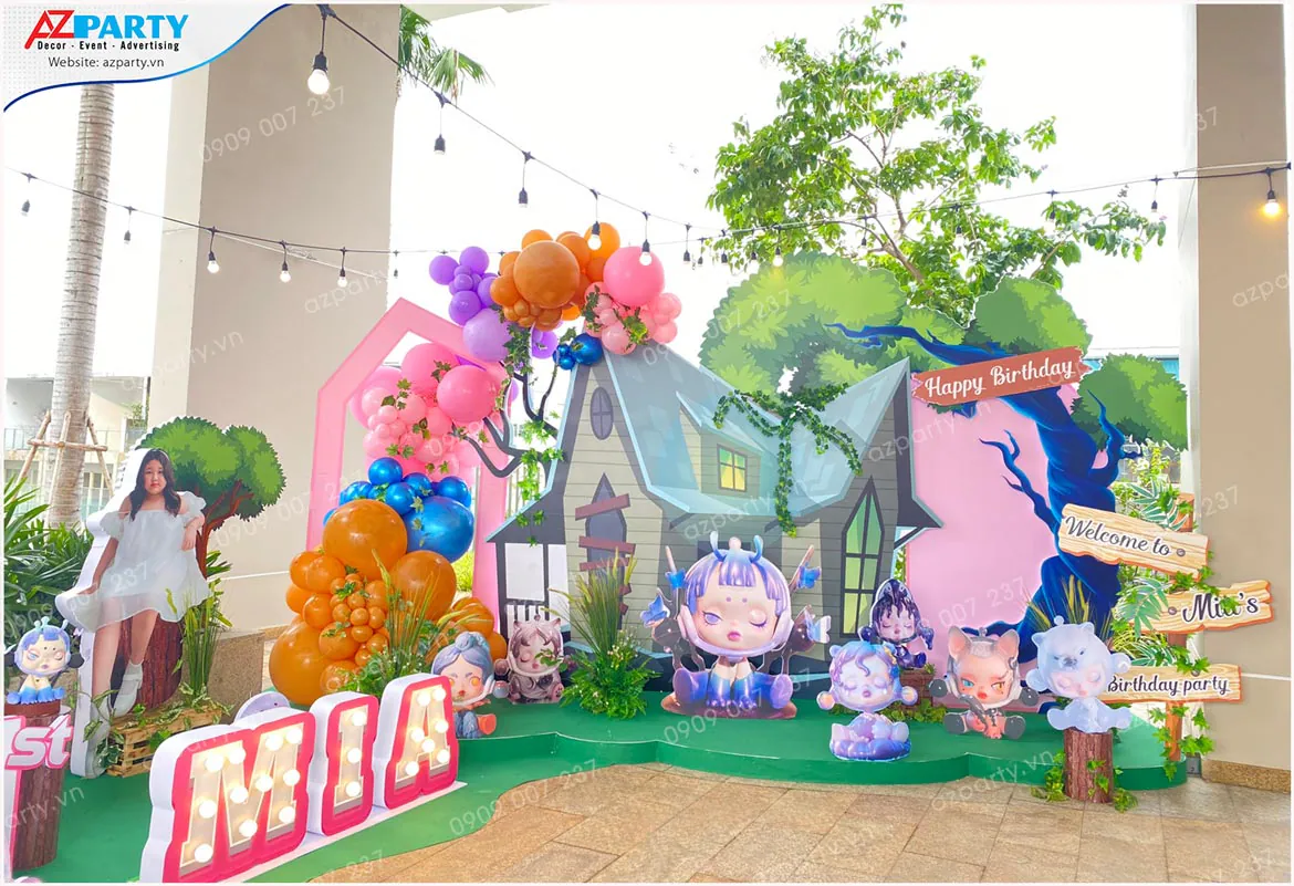 Backdrop mô phỏng ngôi nhà ma quái kỳ ảo cùng cổng bong bóng nghệ thuật nhiều màu sắc và bảng chỉ dẫn Welcome to Mia's birthday party.