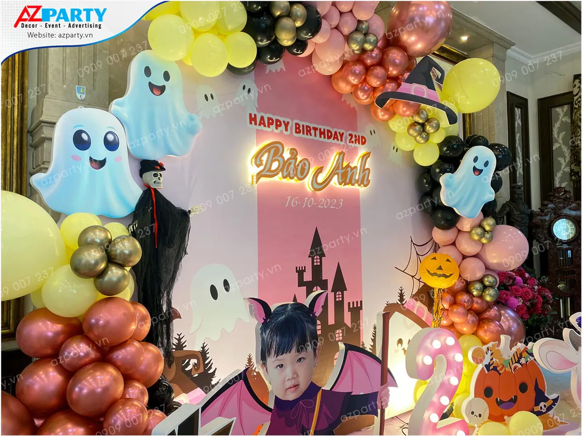 Góc chụp cận cảnh backdrop Halloween trang trí chữ đèn neon tên bé Bảo Anh nổi bật cạnh mô hình ma nhỏ đáng yêu và bộ xương khô.