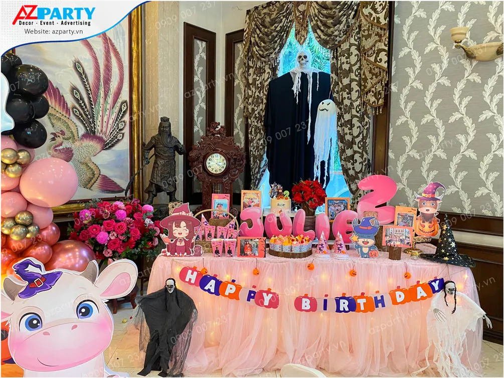 Bàn tiệc ngọt ngào phủ khăn voan hồng lưới lung linh ánh đèn và trưng bày bánh kem sinh nhật, cupcakes theo chủ đề Halloween.