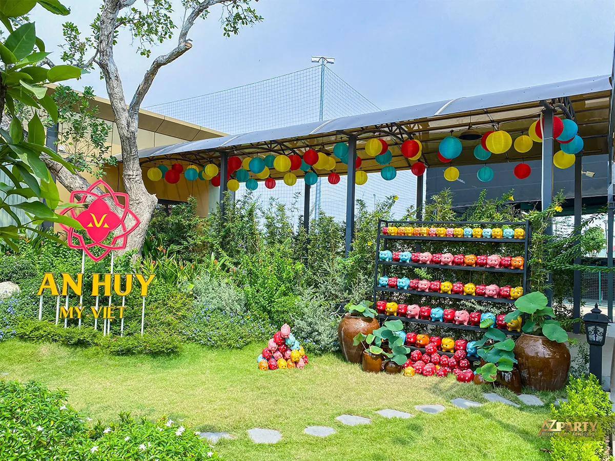 Logo An Huy Mỹ Việt đặt cạnh khu heo đất và lồng đèn trong vườn Tết