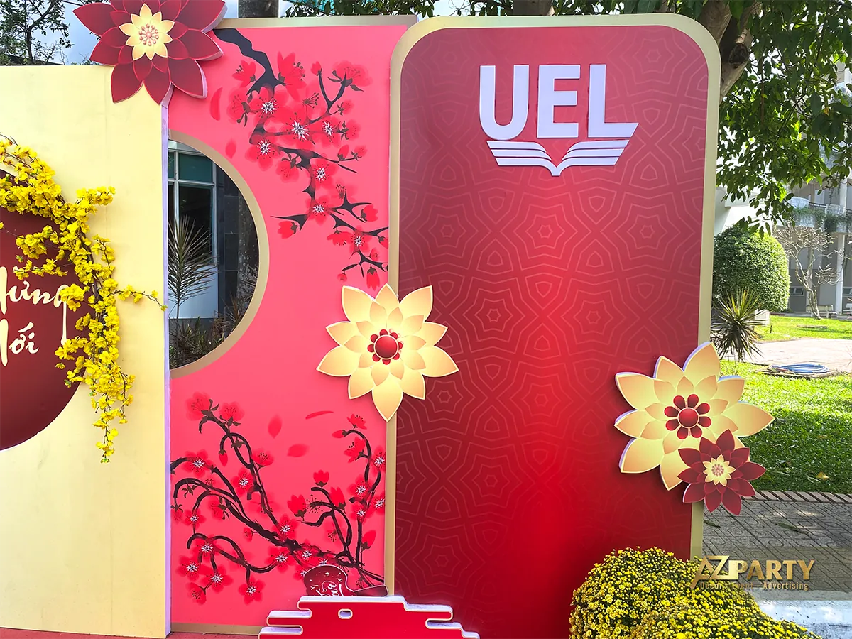 Chi tiết logo UEL giữa các mảng hoa đào, mai vàng và phông trang trí nhiều lớp