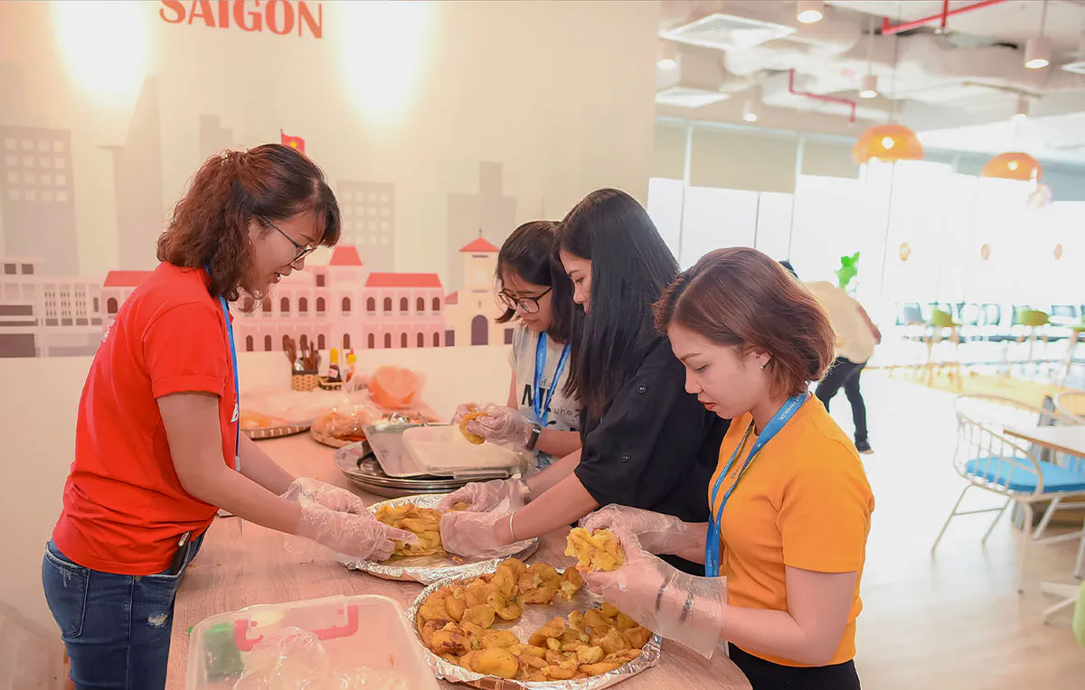 Các nữ nhân viên công ty đeo bao tay nilon đang chuẩn bị các khay đồ ăn nhẹ gồm bánh ngọt và trái cây phục vụ cho mọi người tham gia sự kiện.