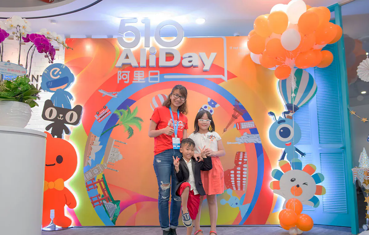 Ba mẹ con cười tươi chụp ảnh lưu niệm cùng nhau trước backdrop sinh nhật sự kiện 510 AliDay đầy màu sắc.