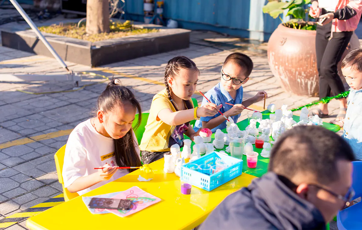 Các bé lớn hơn đang say sưa tô vẽ những bức tượng thạch cao đa dạng tại bàn hoạt động ngoài trời của Ngày hội gia đình.