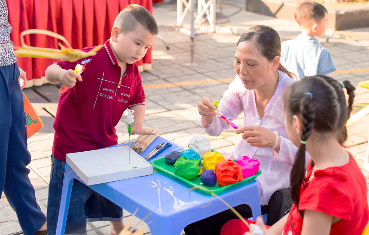 Nghệ nhân nặn tò he mặc áo bà ba trắng đang tỉ mỉ hướng dẫn các bé cách nặn hình tò he truyền thống từ bột màu sặc sỡ.
