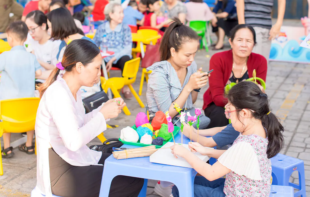 Nghệ nhân nặn tò he đang miệt mài tạo hình các con vật và hoa hồng từ bột màu cho một bé gái tại khu vực trải nghiệm văn hóa dân gian.