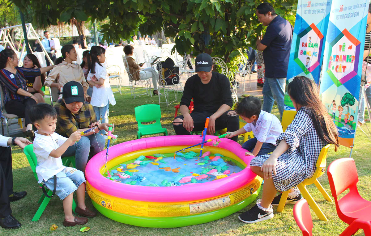 Bố mẹ đang quan sát và hướng dẫn các bé câu cá tại bể phao hơi mini trong khuôn viên rợp bóng cây xanh của KDL Tân Cảng.