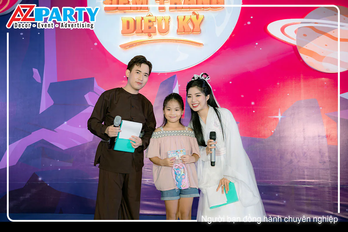 Bé gái xinh xắn cười tươi khi chụp hình kỷ niệm cùng chú Cuội và chị Hằng bên cạnh backdrop.