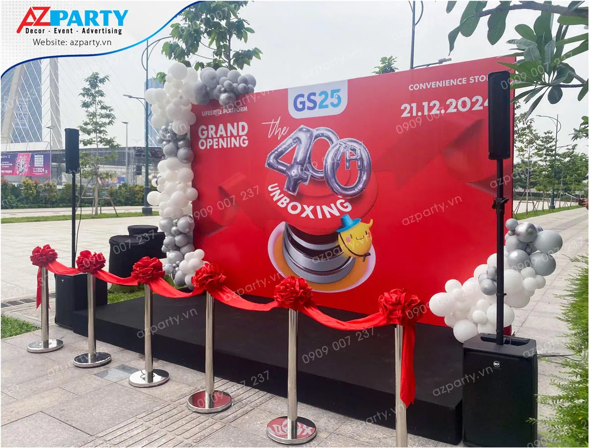 Góc chụp nghiêng sân khấu khai trương GS25 ngoài trời bố trí âm thanh và dải băng đỏ cắt băng.