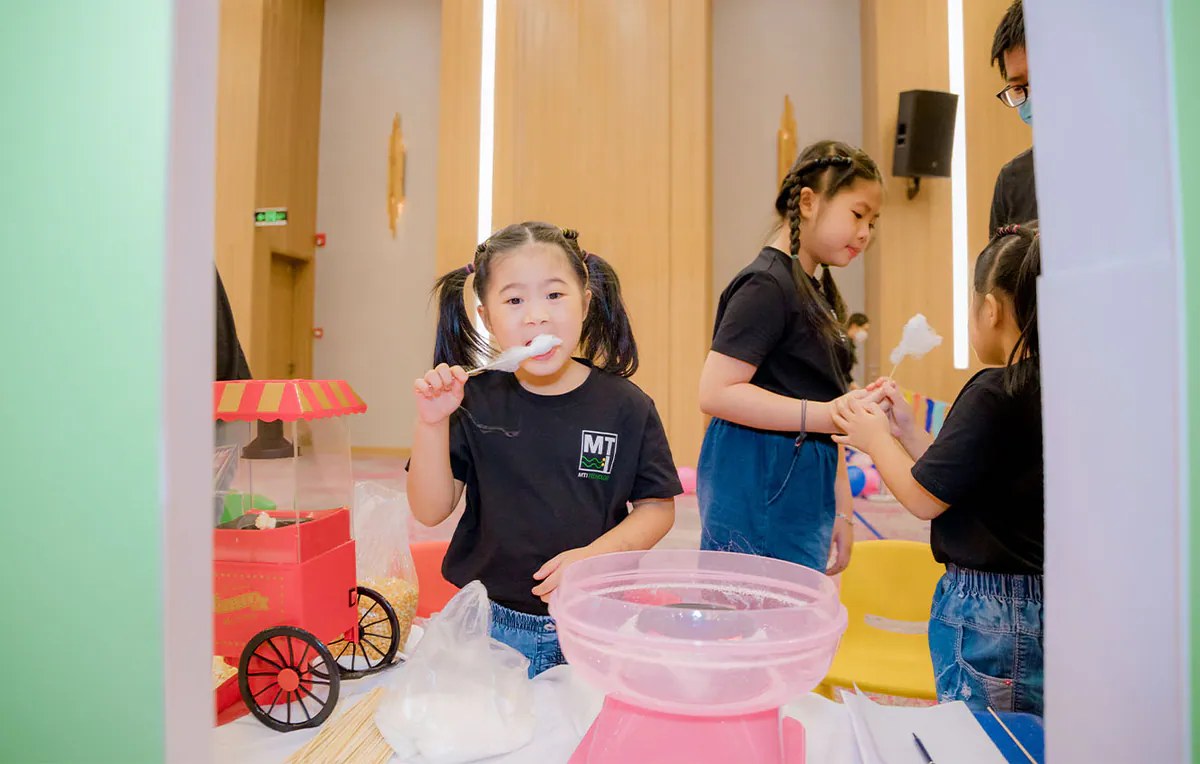 Một bé gái dễ thương buộc tóc hai bên đang vui vẻ ăn kẹo bông gòn ngọt ngào vừa được làm xong từ máy.