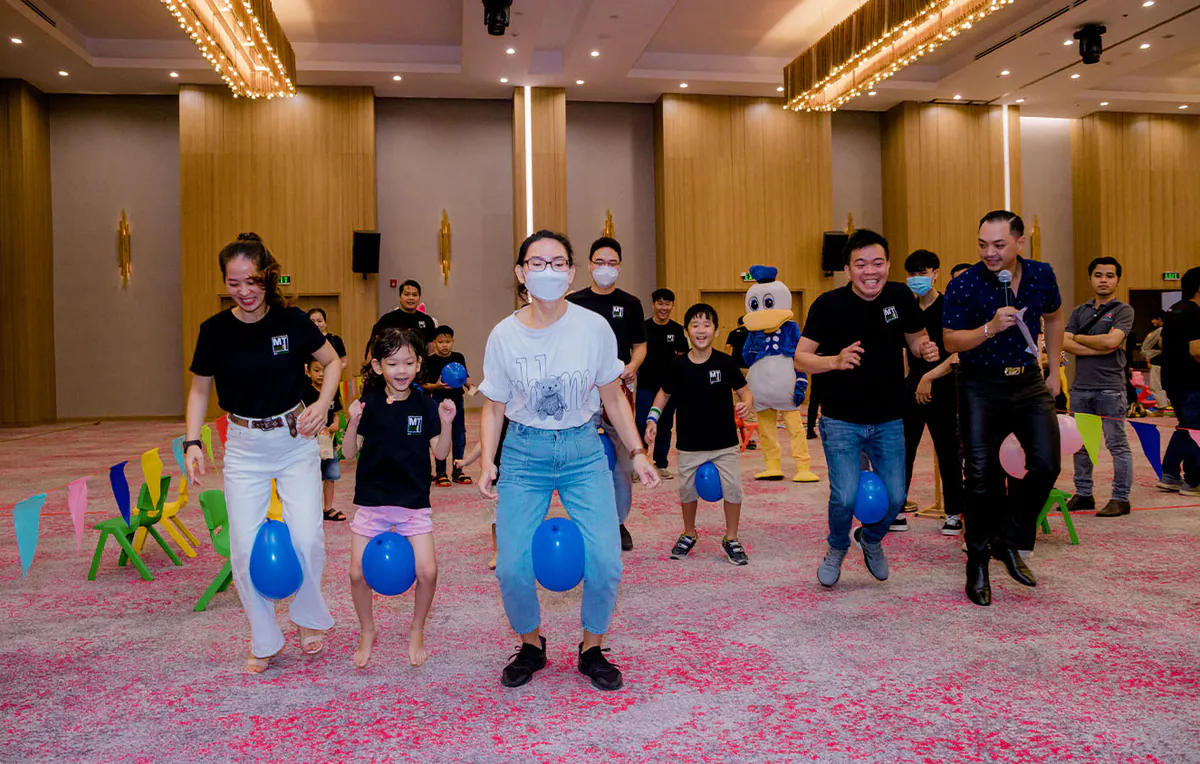 Trò chơi kẹp bóng bay xanh dương di chuyển đầy hào hứng giữa các gia đình tại sảnh tiệc của Holiday Inn.