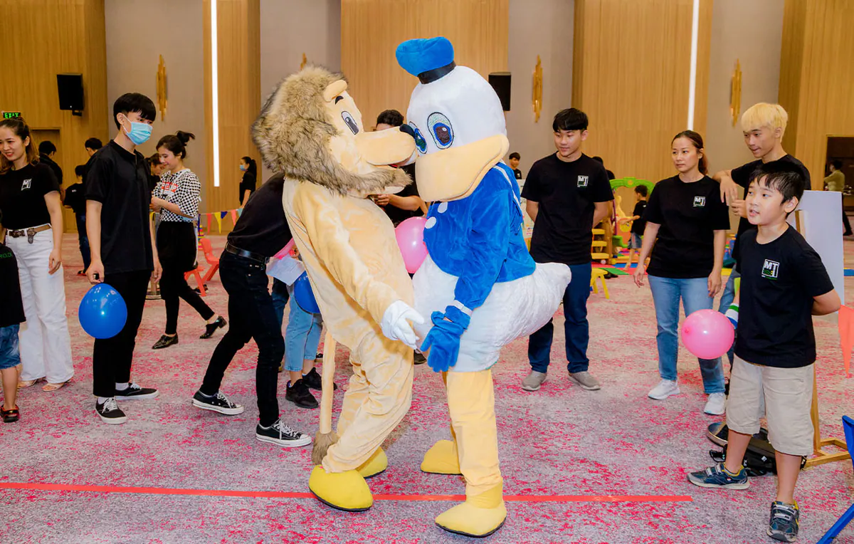Mascot Vịt Donald đeo nơ xanh tinh nghịch tương tác vui nhộn cùng mascot sư tử và các khách mời tham gia sự kiện.