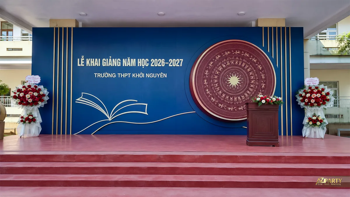 Sân khấu khai giảng THPT Khởi Nguyên màu xanh với trống đồng, sách mở và kệ hoa