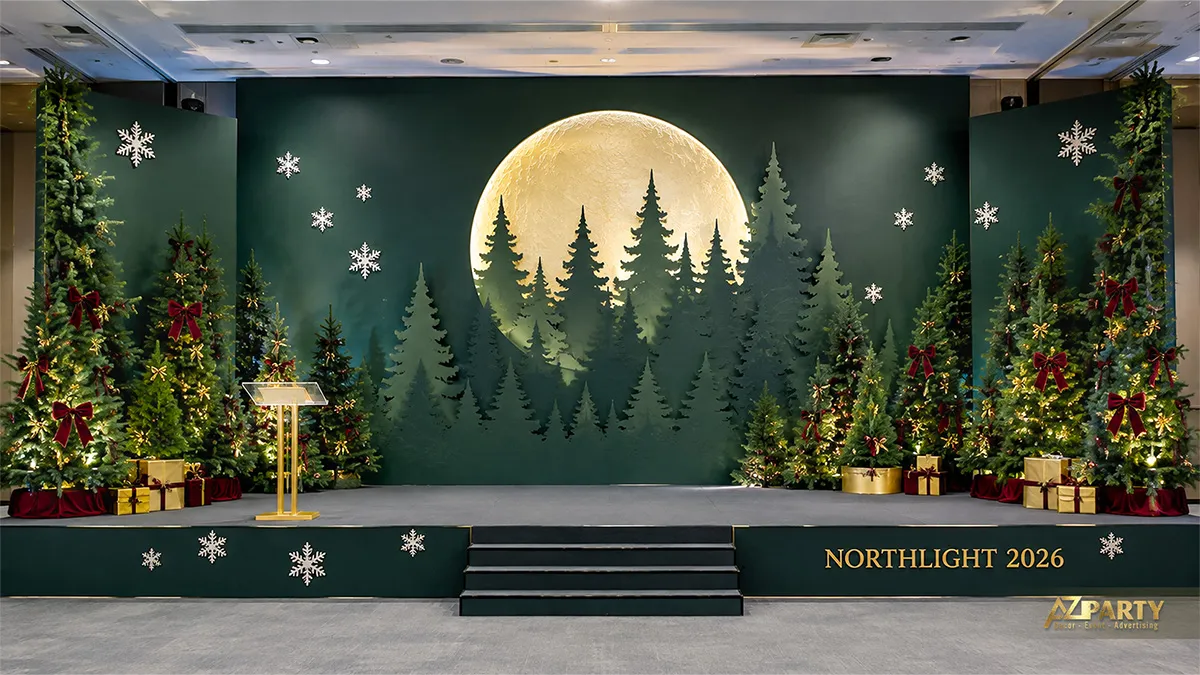 Sân khấu Noel xanh rêu với trăng vàng, rừng thông và hai cụm cây trang trí
