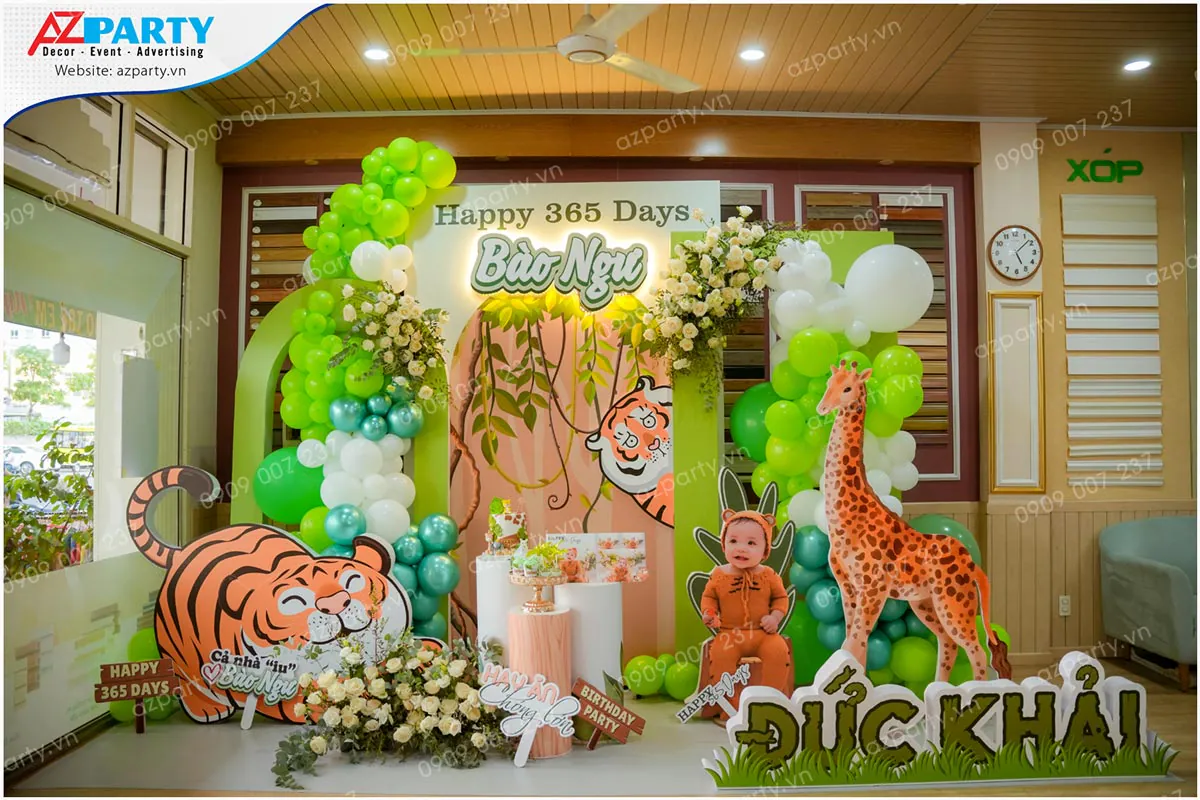 Trang trí thôi nôi tuổi Hổ cho bé Đức Khải (Bảo Ngự) chủ đề rừng xanh với mô hình chú hổ vui vẻ, hươu cao cổ và bóng bay tông xanh lá cây sinh động.